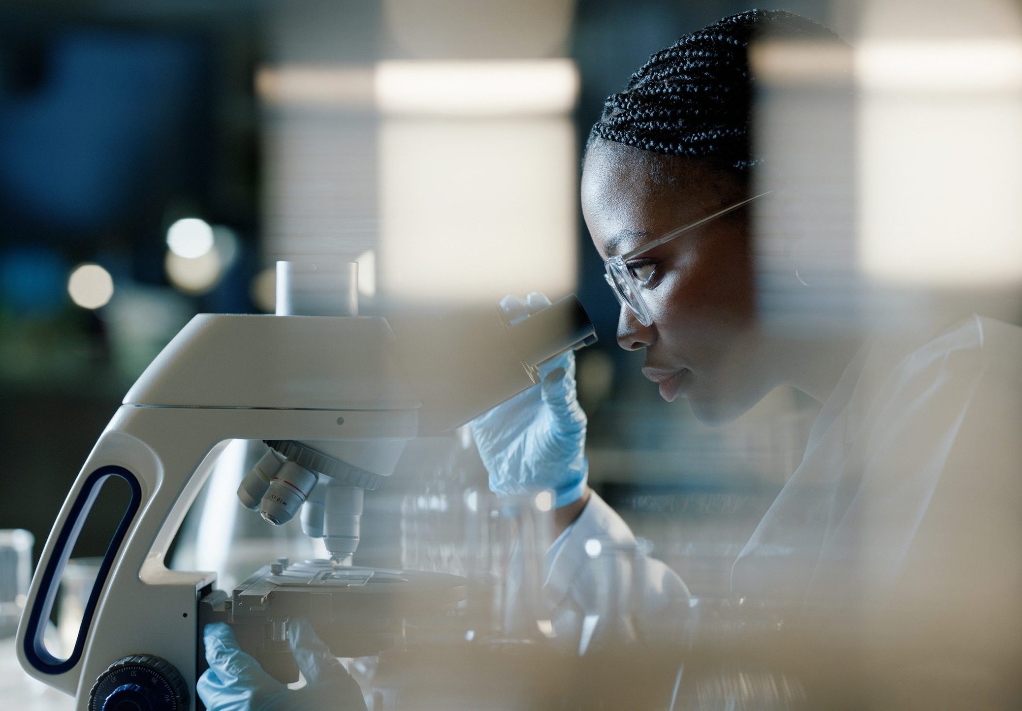 Scientist, microscope and analysis in lab for healthcare, innovation and development in stem cell research. Black woman, investigation and experiment with biotech for dna, exam or test for bacteria